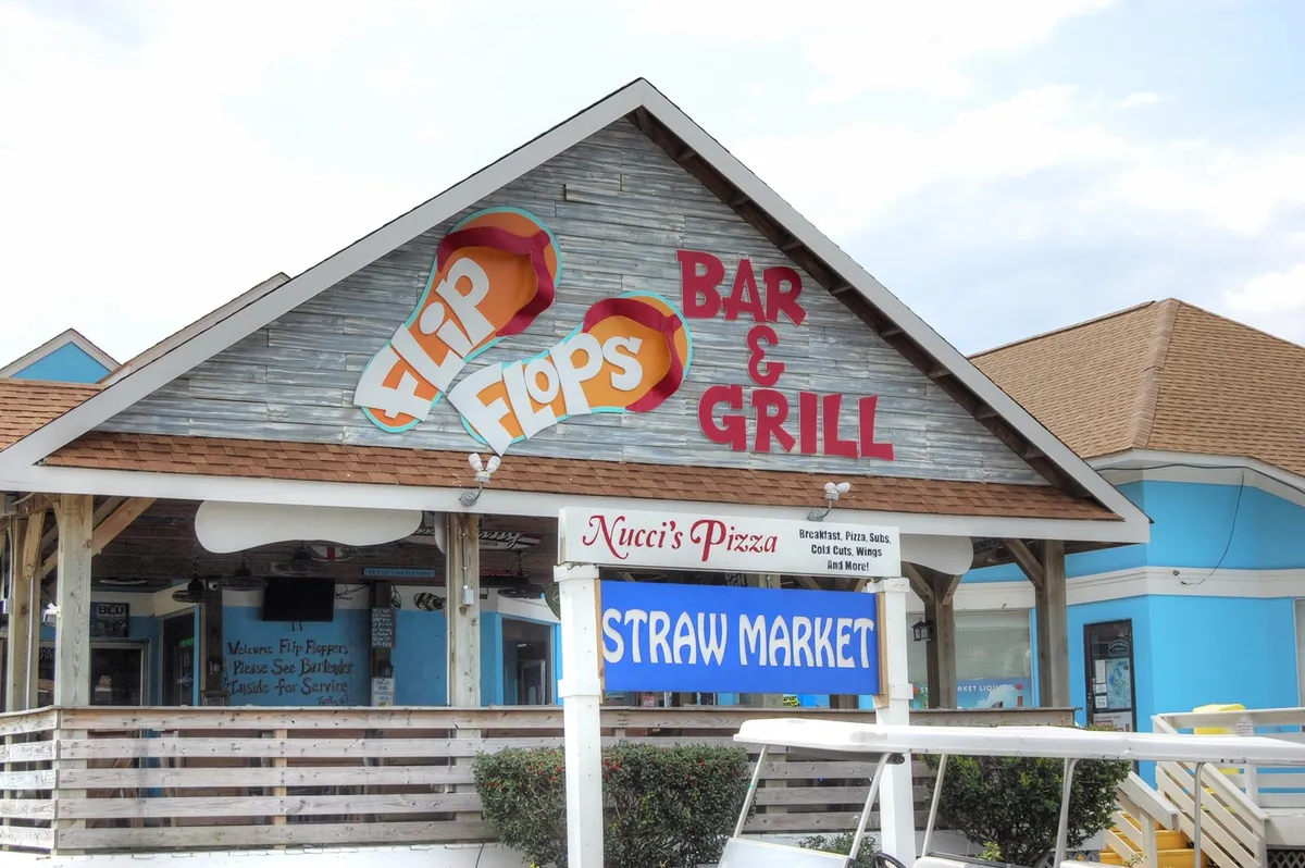 A lively exterior showcasing signs for Flip Flops Bar & Grill, Nucci's Pizzeria, and the Straw Market, all local attractions near Shore Drive. The image hints at casual dining, local flavors, and nearby entertainment, aligning with the section’s mention of upscale dining and evening entertainment.