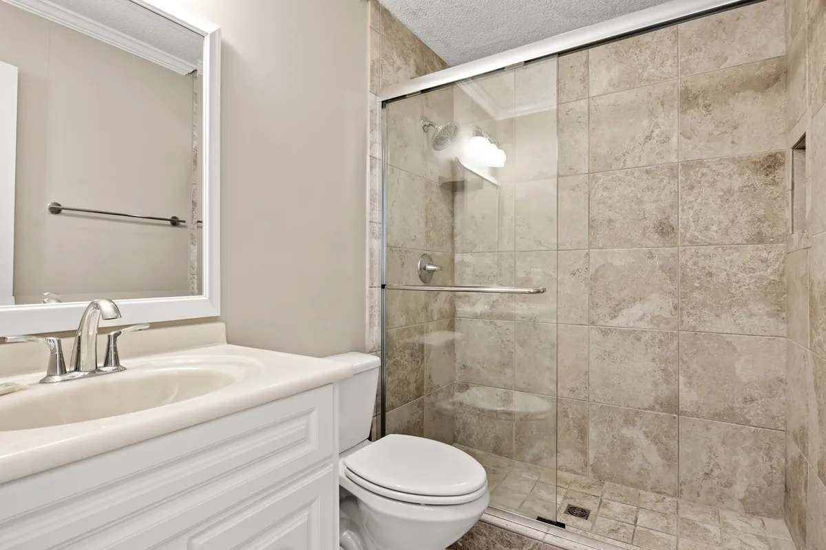 A bright bathroom with a sleek vanity sink, a modern glass shower enclosure, and a wide mirror, creating a calm and refreshing space ideal for morning and evening routines.