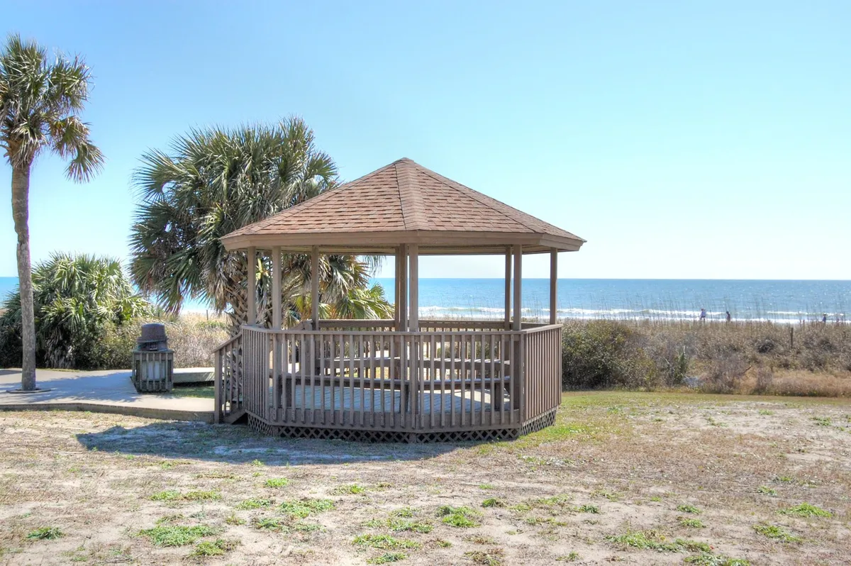 A wooden gazebo overlooks the ocean, framed by palm trees, offering a tranquil spot for relaxation, picnicking, or small social gatherings as the sun rises or sets over the water.