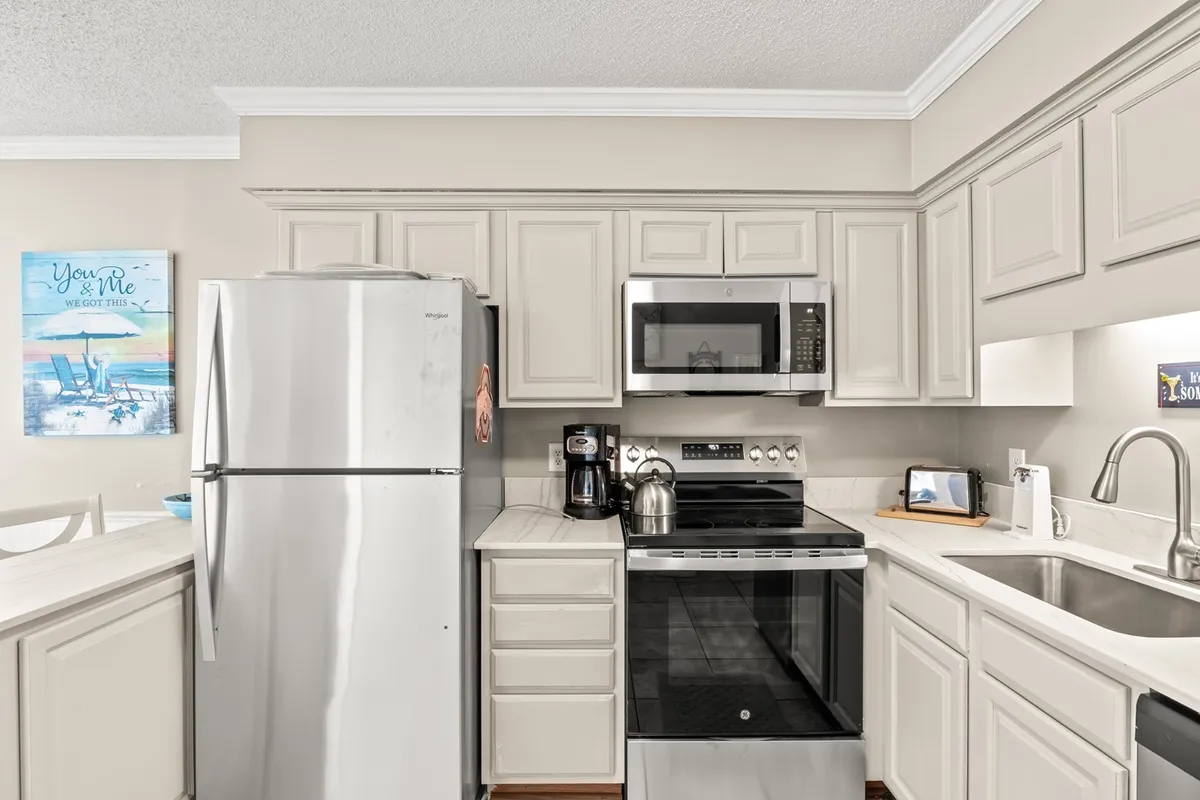 The kitchen is highlighted by a large stainless steel refrigerator, sleek modern stove, spacious kitchen island, and a deep sink. The setting is well-lit and arranged for both cooking and socializing, with clear space for preparing meals or hosting guests.