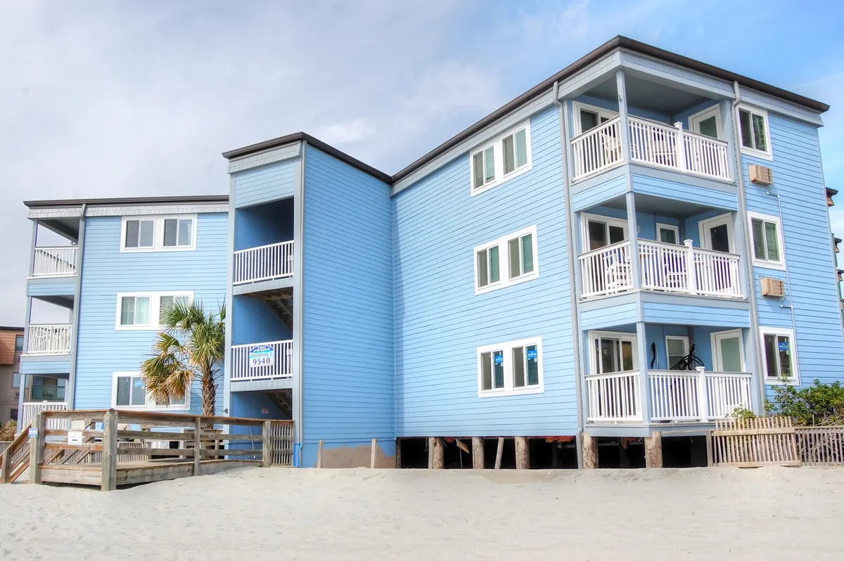 An exterior shot of the building’s blue facade with multiple balconies and a palm tree in the foreground. Balconies are visible, suggesting the building’s relationship with outdoor living and the beach environment.