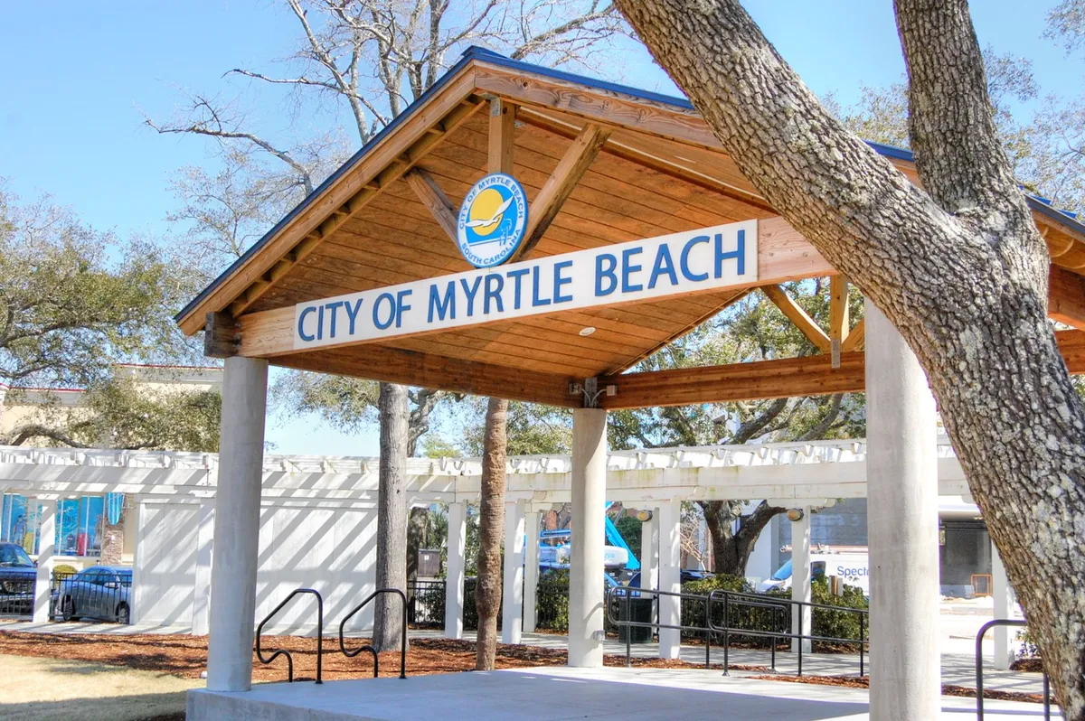 An exterior view of the City of Myrtle Beach signage at a wooden pavilion structure surrounded by trees. The area is designed for community gatherings, local events, and offers scenic views, reinforcing the idea of cultural engagement and neighborly activities.